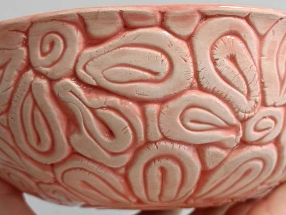 Close-up of the side of a handmade bowl: raised coils and loops under a glossy pink glaze