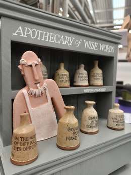 Ceramic ‘Apothecary of Wise Words’ display with a clay shopkeeper figure and small stoneware bottles stamped with famous sayings