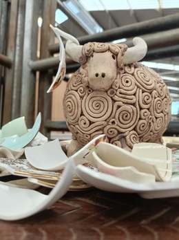 Spiral-textured clay bull sculpture surrounded by broken china in a market hall