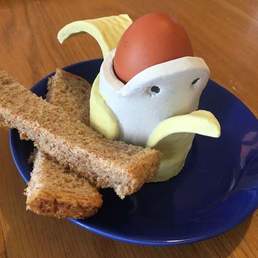 Hand-built clay bird egg cup holding a boiled egg, on a blue saucer with toast soldiers