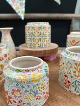 Hand-painted ceramic pots covered in bright floral patterns on a wooden table, by Emily Hett