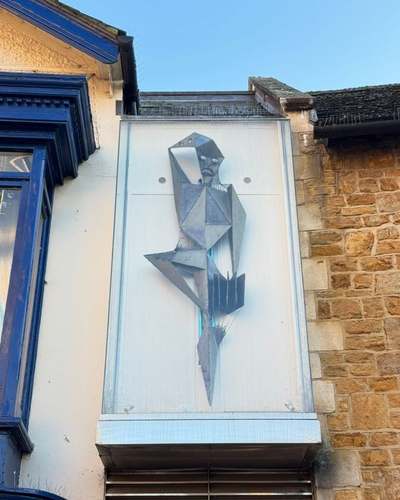 Angular metal Harlequin sculpture on a pale panel beside Harborough Theatre