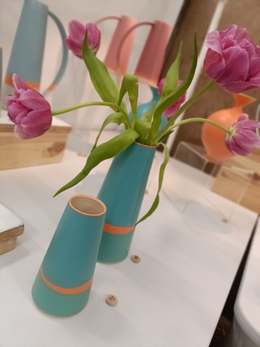 Turquoise ceramic vases with orange bands, one holding pink tulips, on a craft-show display
