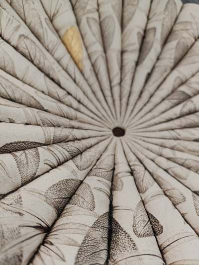 Close-up of a pleated off-white ceramic piece with leaf imprints radiating from the centre and a touch of gold
