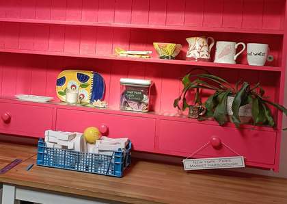 Bright pink dresser with shelves of painted pottery above a wooden work table