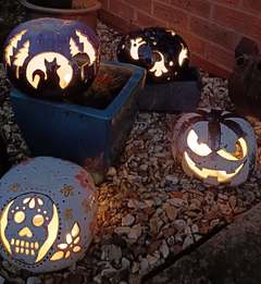 Four glowing hand-carved ceramic pumpkins at dusk, including a black cat and moon design, a sugar skull and a jack-o’-lantern face