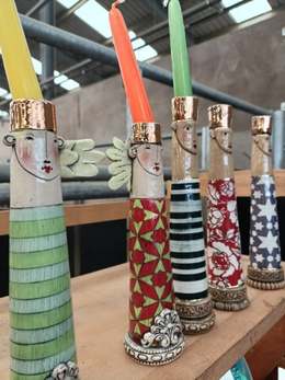 Row of tall ceramic figure candlesticks with gold crowns, painted faces and patterned bodies, by Sarah Saunders