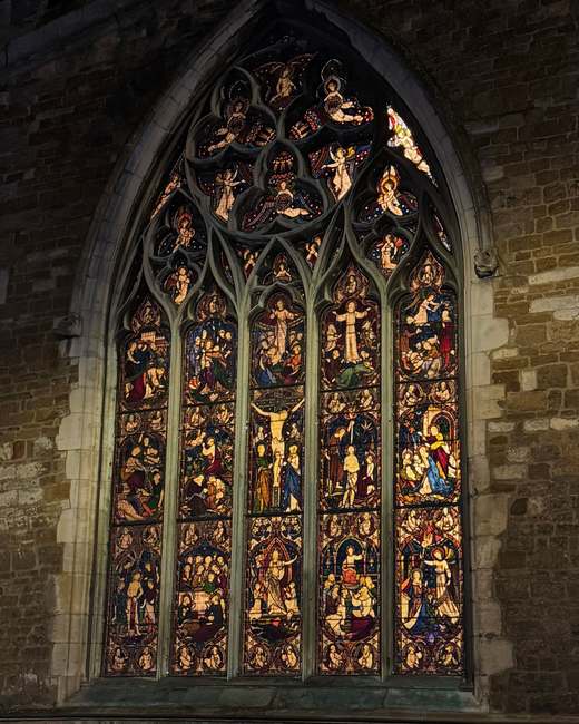 Illuminated stained-glass window of St Dionysius Church at night, showing tiers of biblical figures