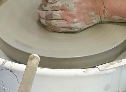Clay-covered hands shaping clay on a pottery wheel